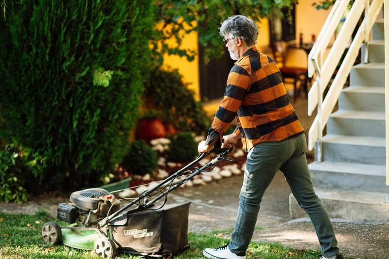 A groundskeeper clearing leaves from the gutter line of a two story rental house