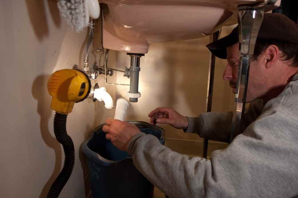 A maintenance technician fitting a new kitchen faucet in an occupied rental unit